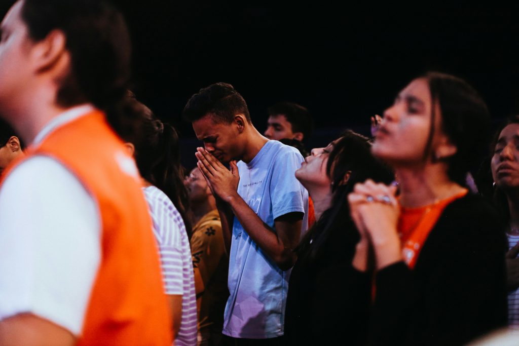 A diverse group of young people praying passionately at a religious gathering.